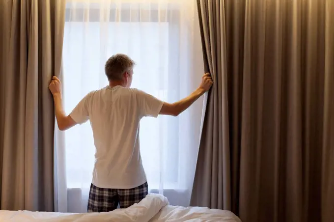 Man opening curtains in hotel room