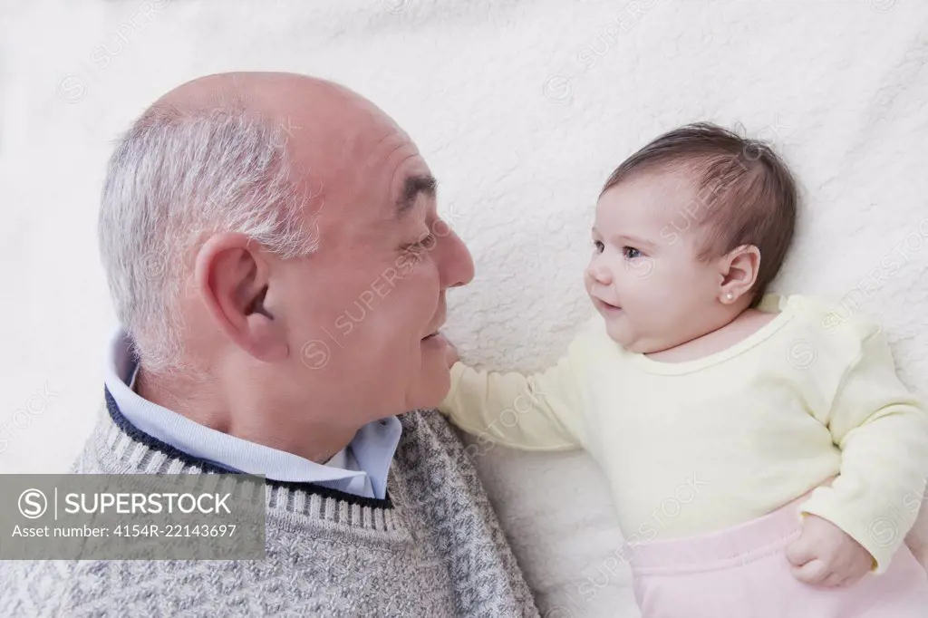 Grandfather Playing with New Baby Granddaughter on Bed