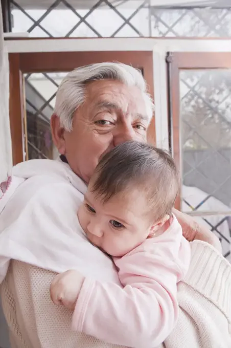 Portrait of a Grandfather Holding New Baby Granddaughter At Home