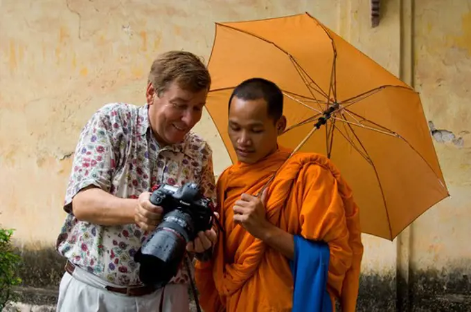 LAOS, VIENTIANE, VAT SISAKET, NOVICE WITH UMBRELLA, TOURIST SHOWING HIM DIGITAL IMAGE