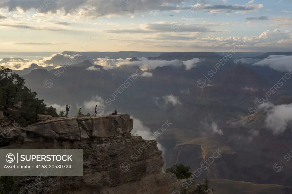 People in evening light on a rock outcrop near Mather Point on the South Rim of the Grand Canyon with clouds clearing after a thunderstorm in the Grand Canyon National Park in northern Arizona, USA.