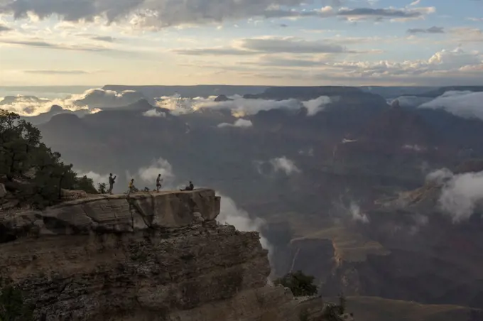 People in evening light on a rock outcrop near Mather Point on the South Rim of the Grand Canyon with clouds clearing after a thunderstorm in the Grand Canyon National Park in northern Arizona, USA.