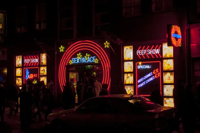 A street scene at night with colorful neon signs of a sex shop in the red light district of Amsterdam in the Netherlands (Holland).