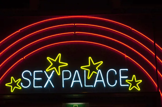 A street scene at night with colorful neon signs of a sex shop in the red light district of Amsterdam in the Netherlands (Holland).