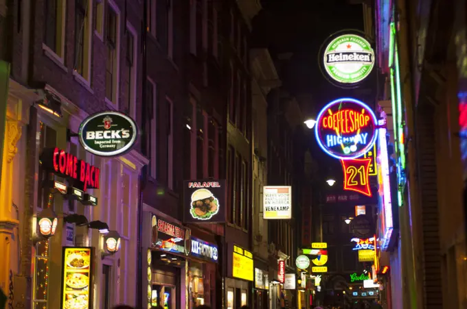 A street scene at night with a coffee shop and colorful neon signs in the red light district of Amsterdam in the Netherlands (Holland).