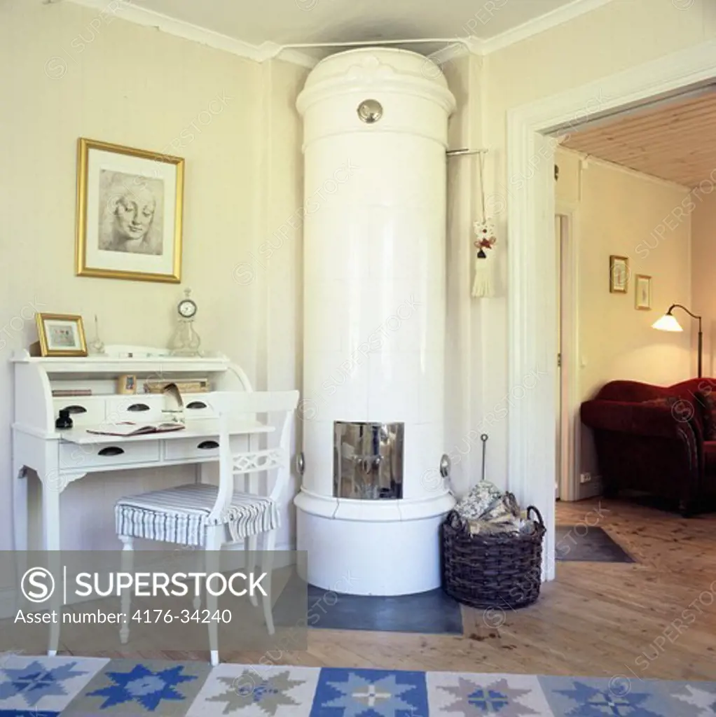 Swedish tiled stove in a livingroom of a cottage with a traditional desk and a red sofa. Sweden