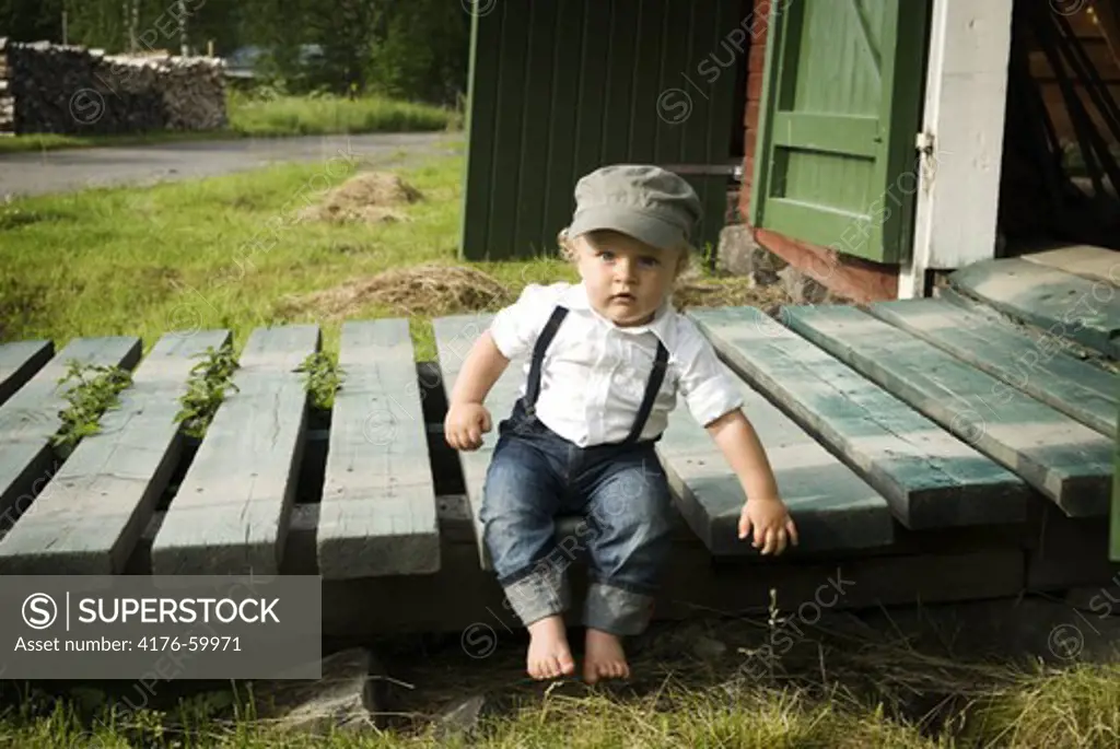 A shild sitting barefoot outside a barn