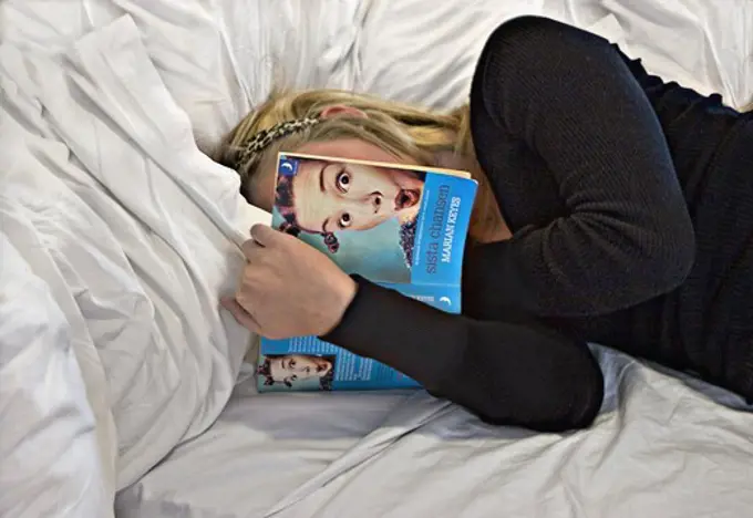 Flicka med mörk tröja ligger i säng och läser
