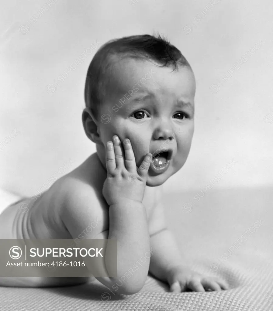 1940S Baby Lying On Stomach With Hand On Cheek & Distressed Look On Face