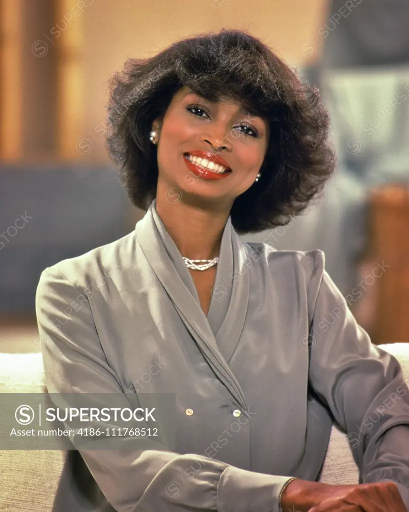 1980s AFRICAN AMERICAN BUSINESS WOMAN SMILING WEAR FASHIONABLE GRAY DRESS LOOKING AT CAMERA