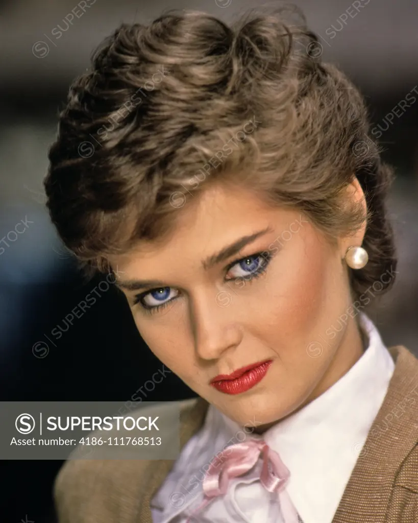 1980s PROVOCATIVE BRUNETTE WOMAN LOOKING AT CAMERA WEARING WHITE BLOUSE PINK RIBBON TIE TAN JACKET PEARL EARRINGS RED LIPSTICK