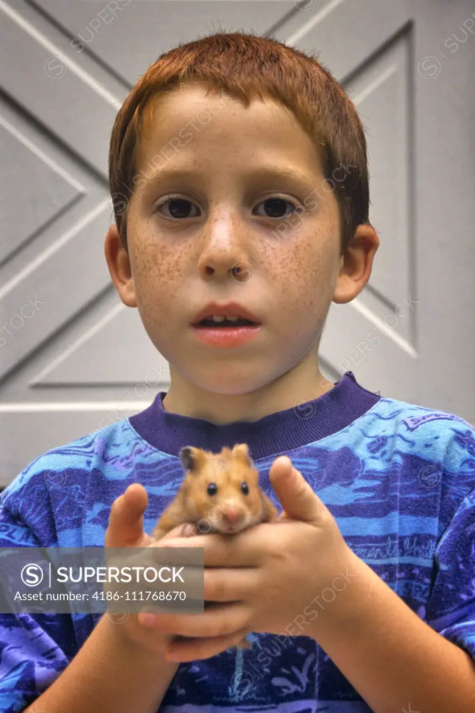 FRECKLE-FACED BOY HOLDING  PET HAMSTER IN HIS HANDS LOOKING AT CAMERA