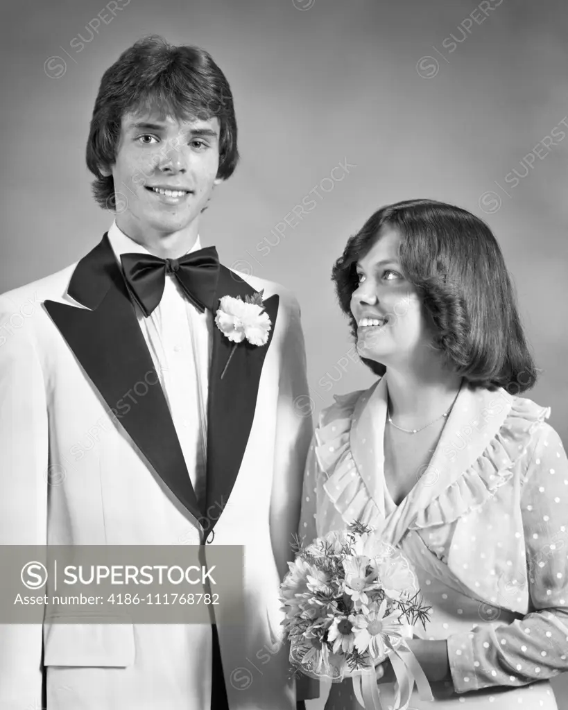 1970s TEEN COUPLE DRESSED UP FOR PROM DANCE FORMAL ATTIRE GIRL HOLDING BOUQUET LOOKING UP AT TALL BOY