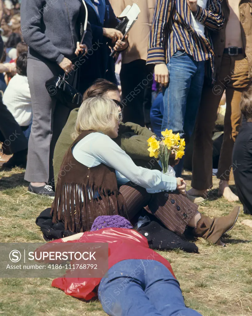 1960s BLONDE WOMAN IN FRINGED VEST HOLDING YELLOW DAFFODILS AMIDST CROWD 1969 PEACE RALLY FAIRMONT PARK PHILADELPHIA PA USA