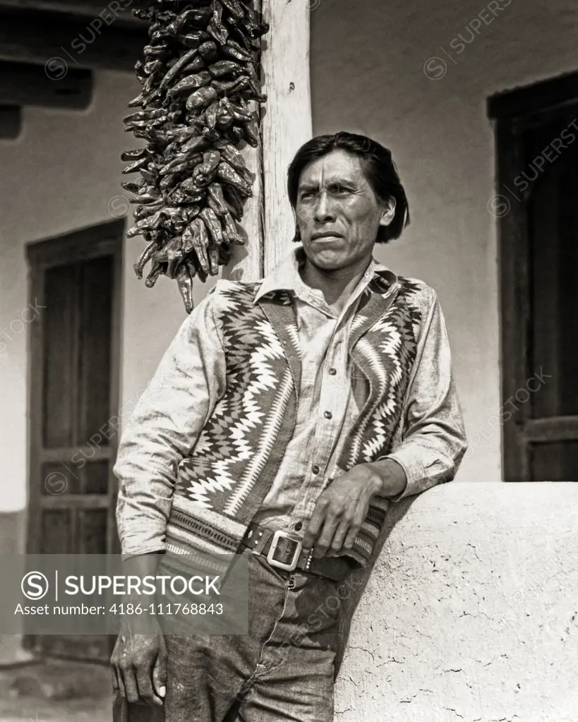 1930s PORTRAIT NATIVE AMERICAN INDIAN MAN WEARING WOVEN VEST STANDING OUTSIDE ADOBE HOME SAN ILDEFONSO PUEBLO NEW MEXICO USA