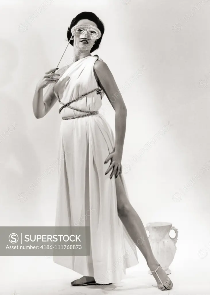 1950s BRUNETTE WOMAN WEARING LONG WHITE GRECIAN DRESS COSTUME HOLDING MASK TO EYES LOOKING AT CAMERA