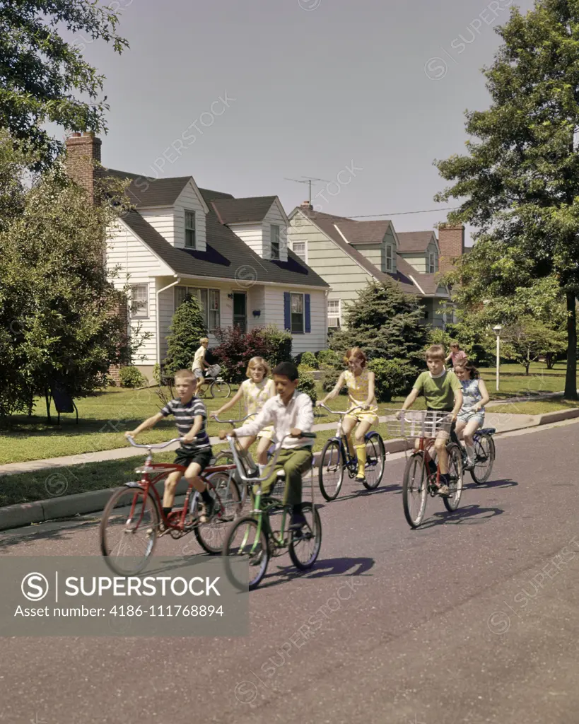 1960s 1970s GROUP CHILDREN RIDING BIKES DOWN SUBURBAN STREET