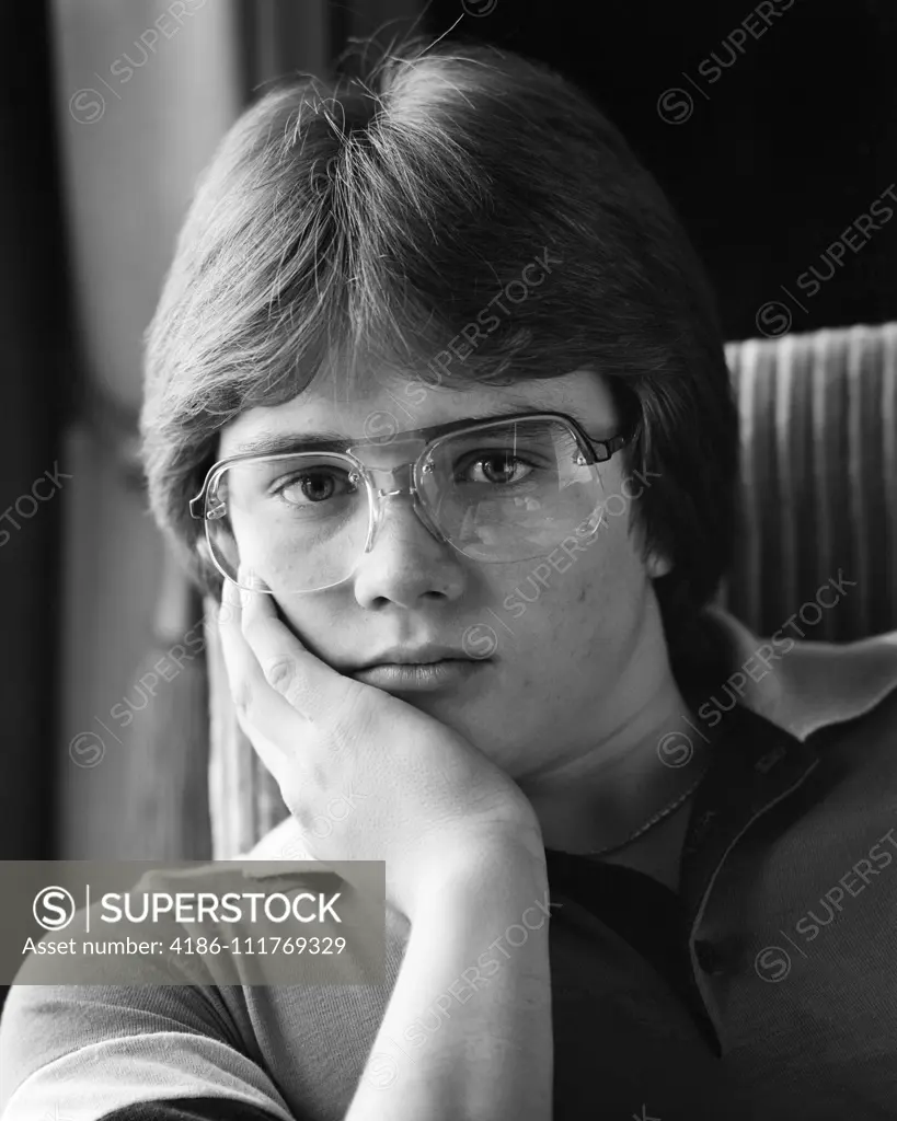 1980s PORTRAIT TEEN BOY LOOKING AT CAMERA WEARING AVIATOR FRAME EYEGLASSES WITH AN UNEMOTIONAL FACIAL EXPRESSION