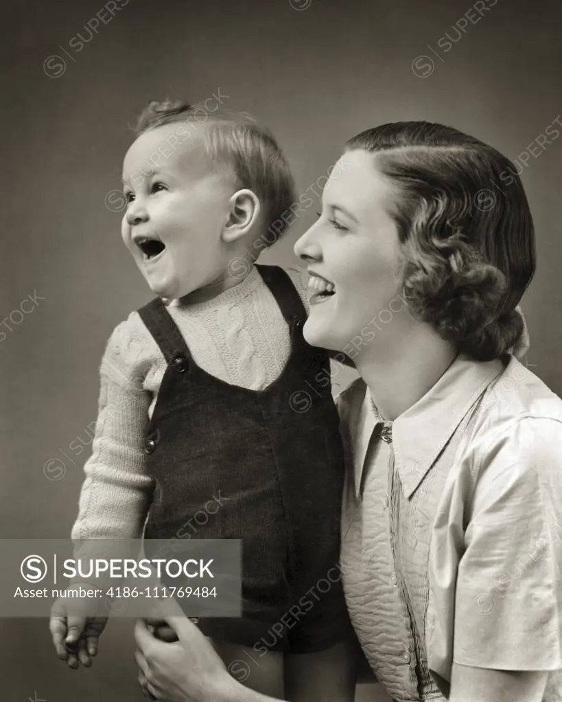 1940s LAUGHING BABY BOY TODDLER STANDING SUPPORTED BY SMILING MOTHER