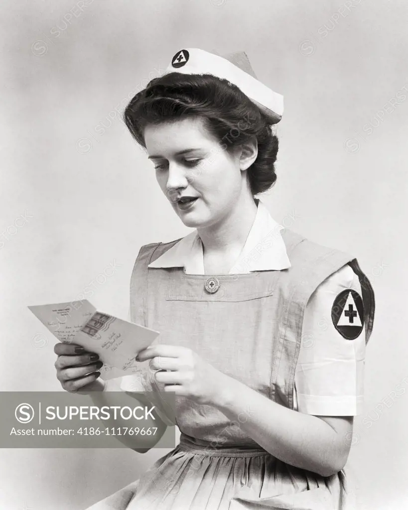 1940s WOMAN SERVING VOLUNTEER RED CROSS NURSE WEARING UNIFORM SMOCK DRESS AND CAP READING LETTER DURING WORLD WAR 2
