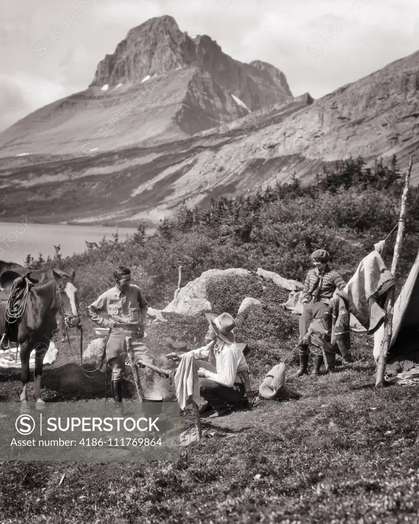 1920s THREE PEOPLE EASTERN VACATION COUPLE AND WESTERN COWBOY COOK AT CAMPSITE BY BAKER LAKE BANFF NATIONAL PARK ALBERTA CANADA