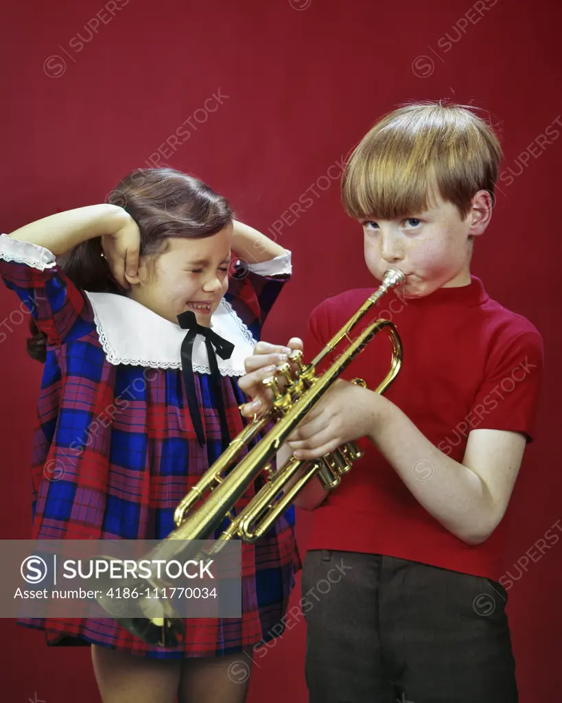 1970s 1980s LITTLE GIRL SISTER CLOSING EYES COVERING EARS HEARING LISTENING TO OLDER BOY BROTHER PRACTICING PLAYING TRUMPET