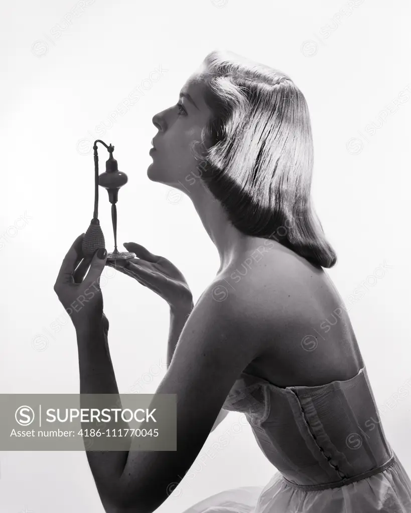 1950s PROFILE PORTRAIT STYLISH ELEGANT YOUNG WOMAN HOLDING UP PERFUME ATOMIZER SPRAY BOTTLE