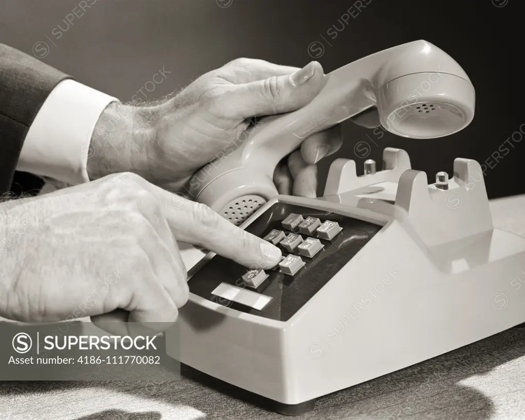 1960s MAN HANDS ONLY LIFTING THE RECEIVER HEAD SET OF TELEPHONE WITH LEFT HAND AND DIALING ON PUSH-BUTTON DIGITS WITH RIGHT HAND