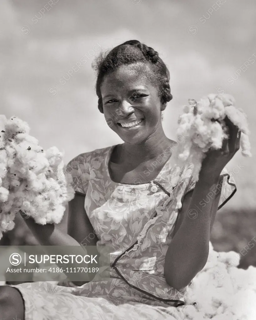 1930s SMILING AFRICAN AMERICAN YOUNG WOMAN SHARECROPPER LOOKING AT CAMERA HOLDING UP TWO HANDFULS OF PICKED COTTON LOUISIANA USA