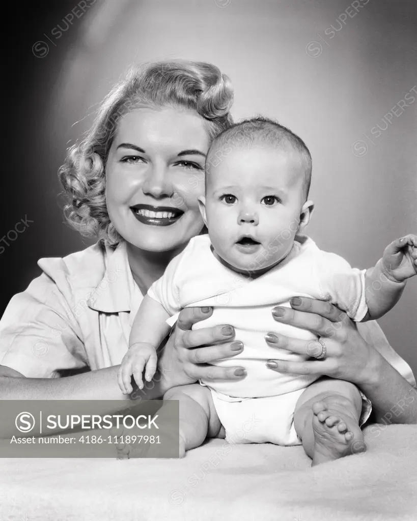 1950s BLONDE MOTHER HOLDING BABY GIRL BOTH LOOKING AT CAMERA