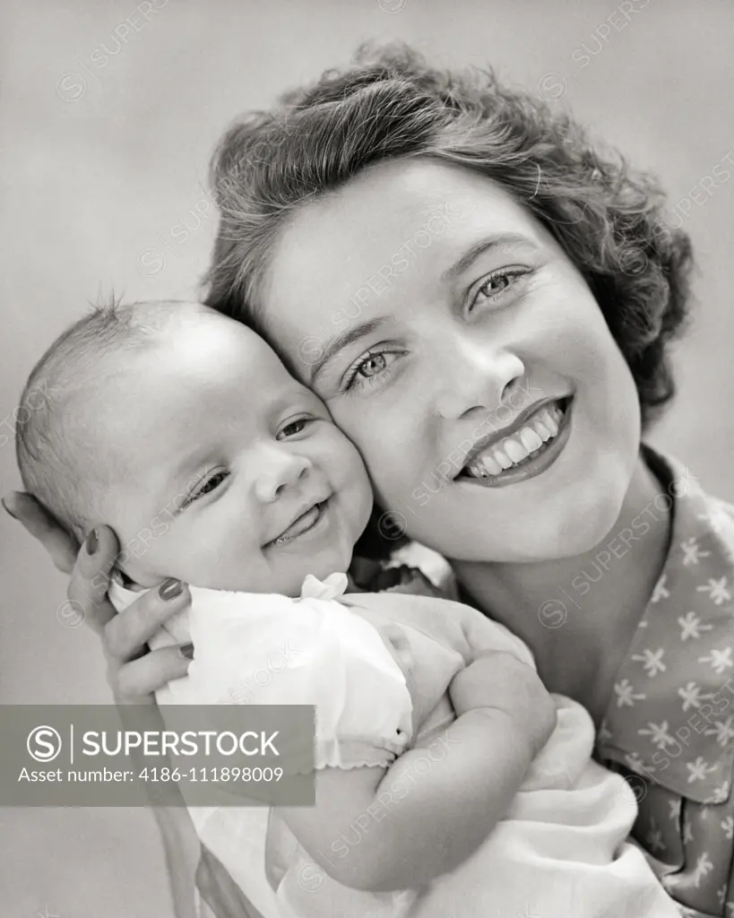 1940s PORTRAIT OF SMILING MOTHER LOOKING AT CAMERA HOLDING BABY DAUGHTER CHEEK TO CHEEK