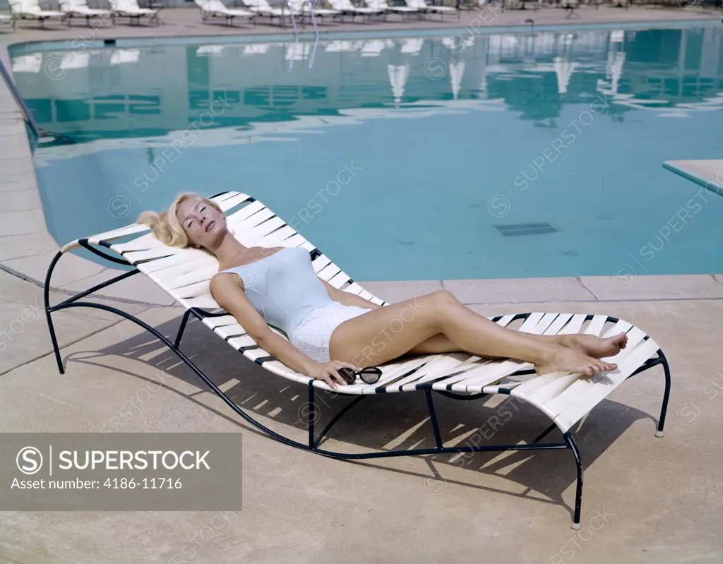 1960S Elegant Tall Blond Woman In Bathing Suit Reclining On A Lounge Chair By Swimming Pool Tanning In The Sunshine