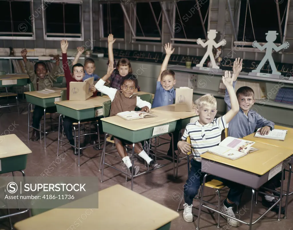 1960S Elementary School Children In Classroom With Hands Raised To Answer Question