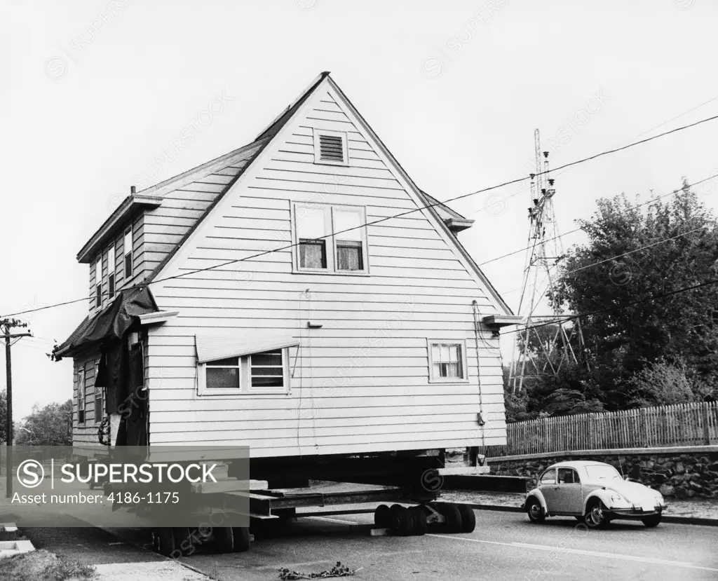 1970S Volkswagen Beetle Automobile Passing House Being Moved On Wheels Along Street