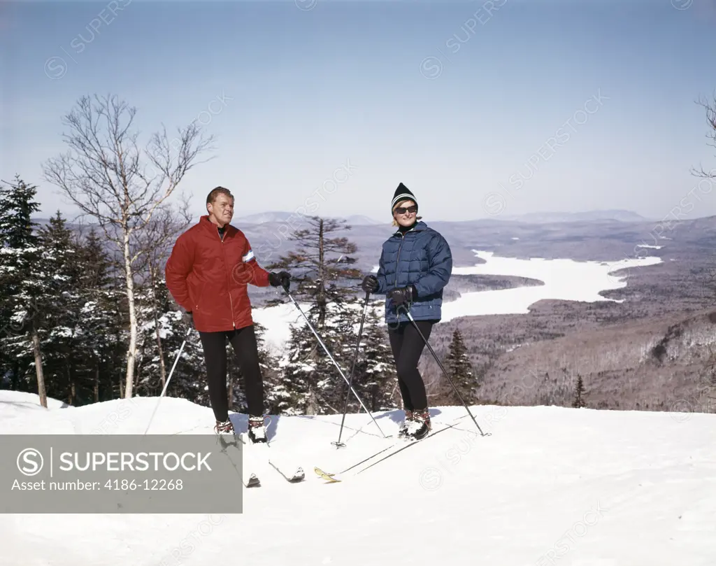 1960S Couple Man Woman Skiers Standing Top Of Hill With Vista View Winter Lake