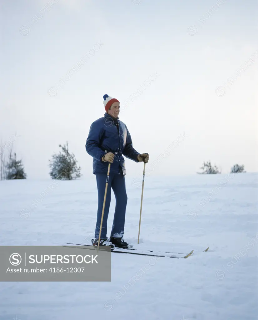 1970S Full Length Man Standing Wearing Blue Jacket Wool Cap Skis Ski Poles