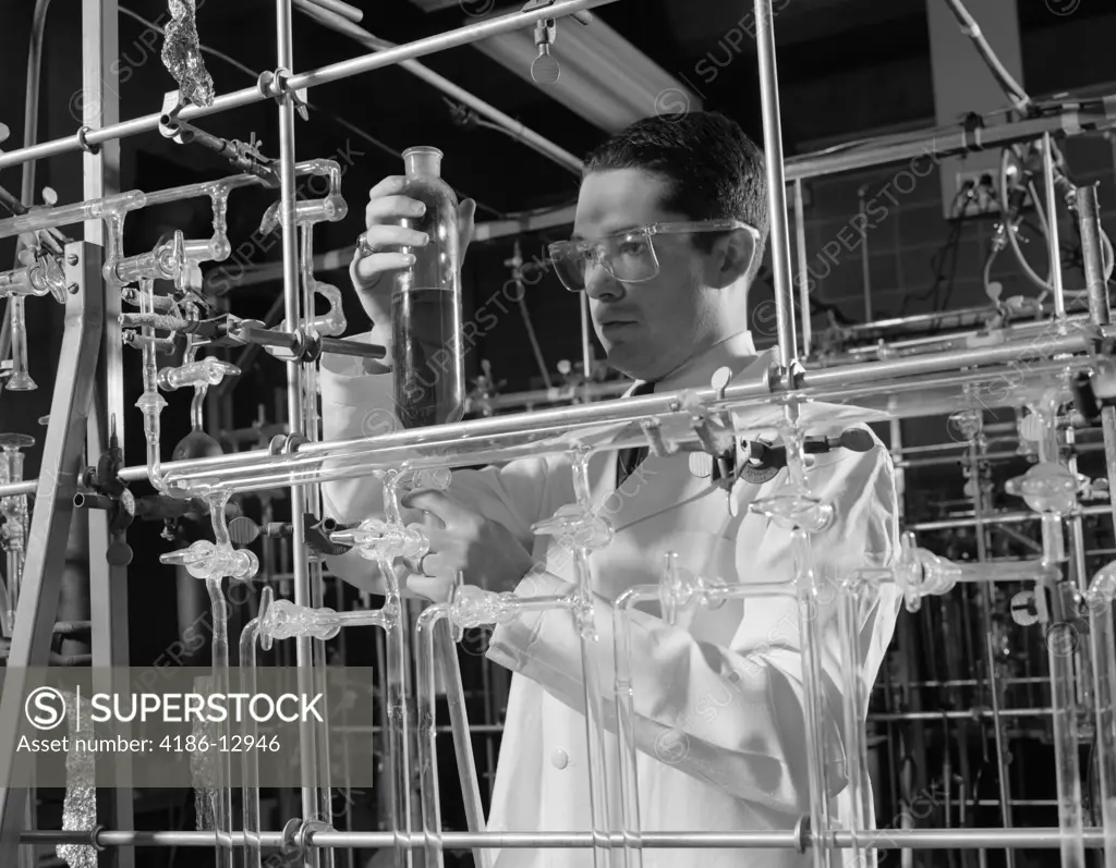 1960S Man In Lab Coat & Goggles Surrounded By Glass Tubing Conducting Scientific Research