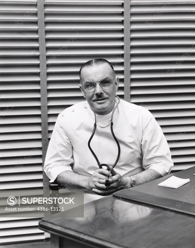 1940S Portrait Of Doctor Sitting Behind Desk Smiling