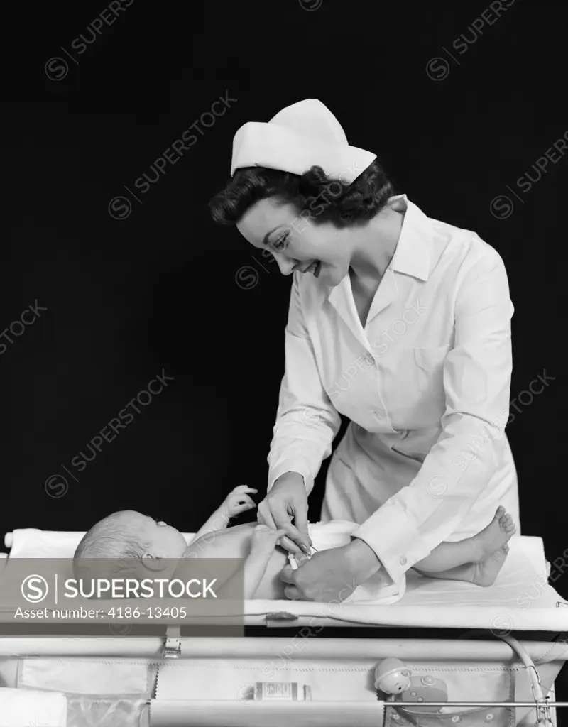 1940S Smiling Woman Nurse Changing Baby Diaper In Nursery