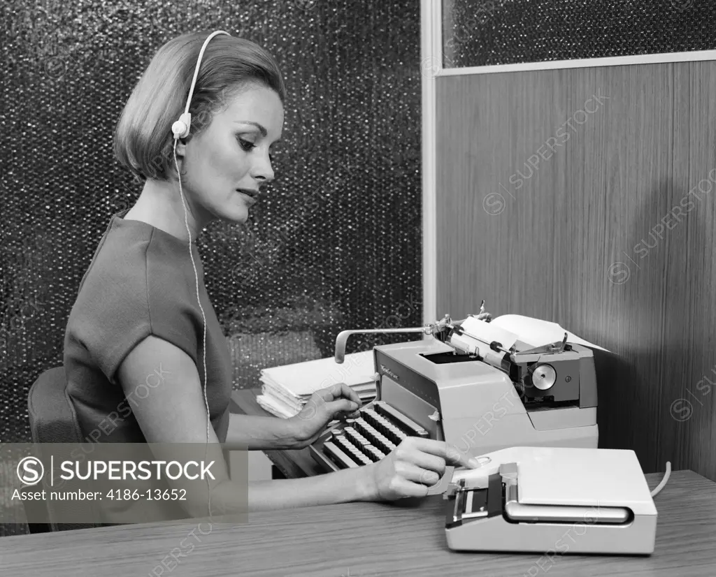 1960S Side View Of Secretary At Desk Behind Typewriter Wearing Headset & Turning Knob On Dictaphone