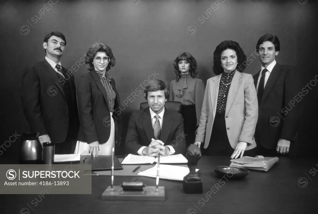 1980S Group Portrait Of Office Staff Standing Behind Desk Around Boss With Serious Expressions