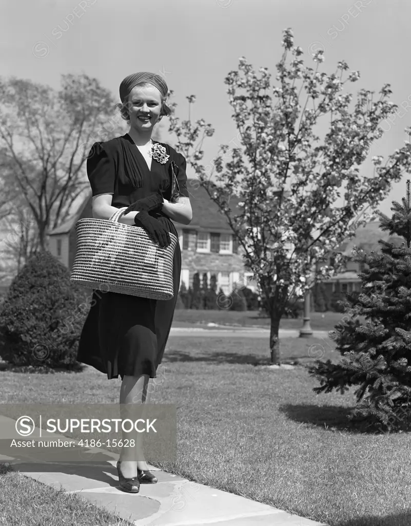 1930S 1940S Stylishly Dressed Woman Walking Down Suburban Street Carrying Straw Bag  