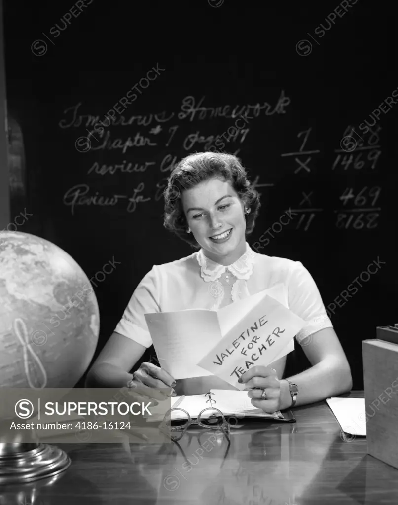 1950S Teacher Reading Valentine Card At Desk With Blackboard In Background