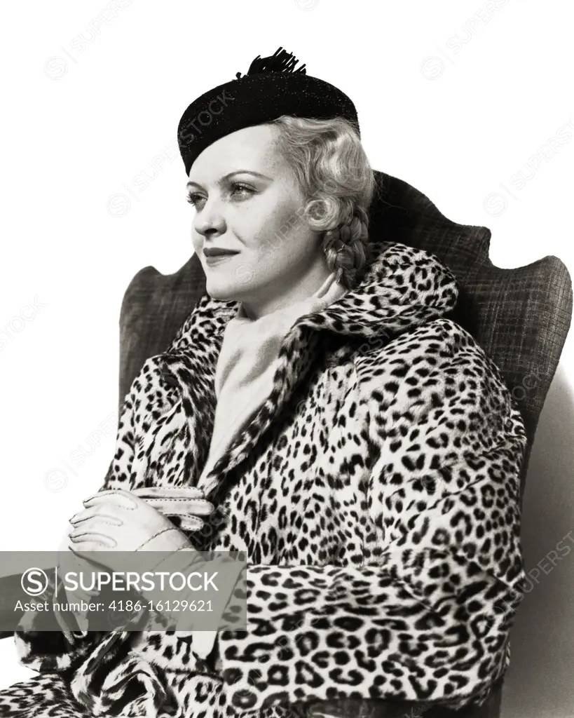 1930s ELEGANT BLONDE WOMAN SITTING IN CHAIR WEARING HAT LEATHER GLOVES AND LEOPARD SKIN COAT