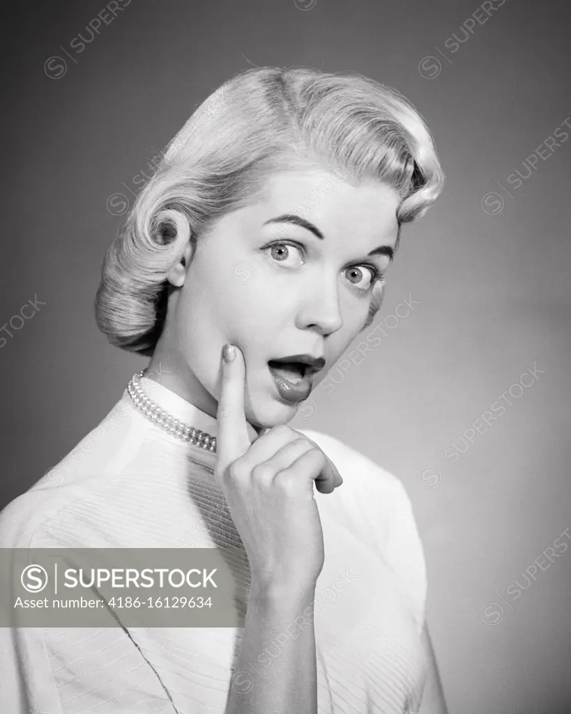 1950s BLONDE WOMAN PAGE BOY HAIR STYLE PEARL NECKLACE WHITE BLOUSE FINGER TOUCHING FACE THOUGHTFUL EXPRESSION LOOKING AT CAMERA