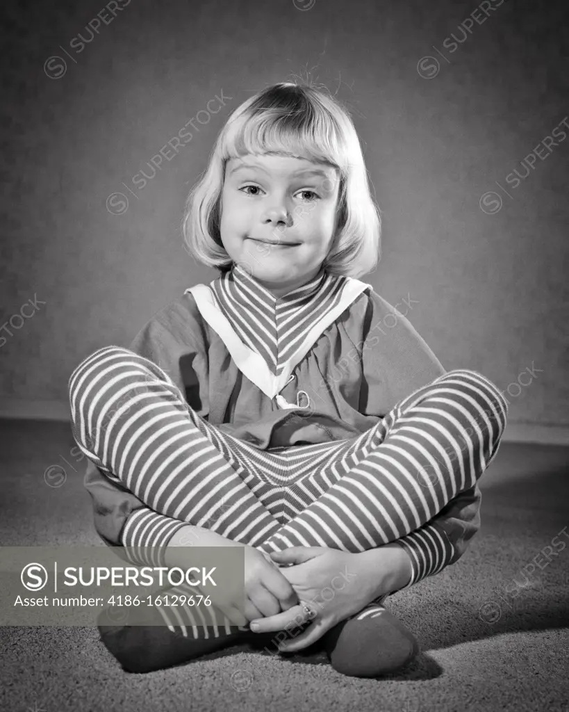 1950s 1960s SMILING BLOND GIRL QUIZZICAL FACIAL EXPRESSION SITTING CROSS LEGGED LOOKING AT CAMERA WEARING STRIPED LEOTARD TIGHTS