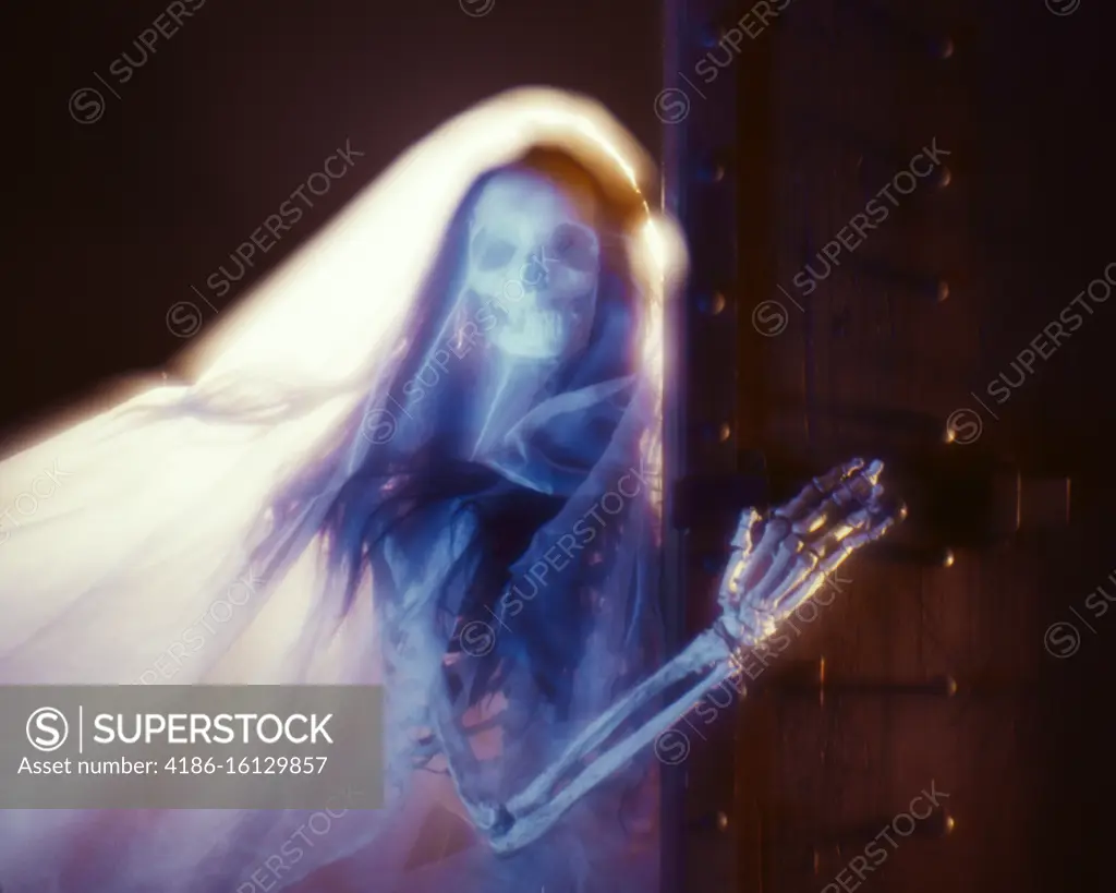 1970s SPOOKY SYMBOLIC SKELETON OF WOMAN WITH LONG HAIR WITH VEIL OR SHROUD LOOKING AT CAMERA BONY HAND PUSHING OPEN A DOOR 