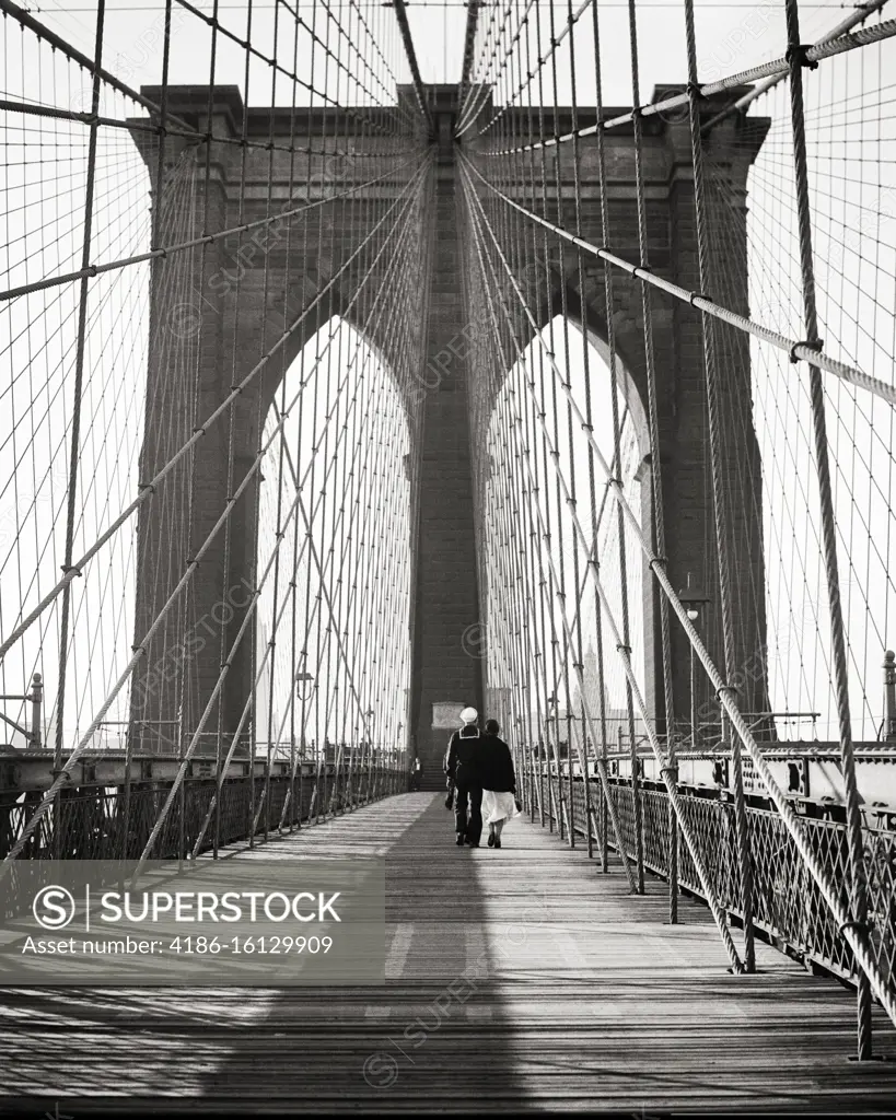 1940s BACK VIEW OF COUPLE MAN USN SAILOR IN UNIFORM WITH HIS ARM AROUND WOMAN WALKING ON THE BROOKLYN BRIDGE NEW YORK CITY USA