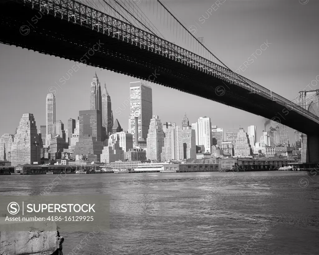 1960s DOWNTOWN FINANCIAL DISTRICT NEW YORK CITY FROM UNDER BROOKLYN BRIDGE OVER THE EAST RIVER