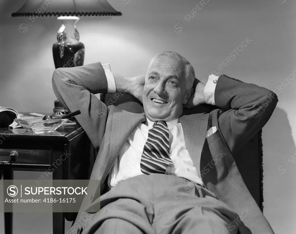 1950S Older Man Lounging In Chair Wearing Suit Arms Behind Head - SuperStock